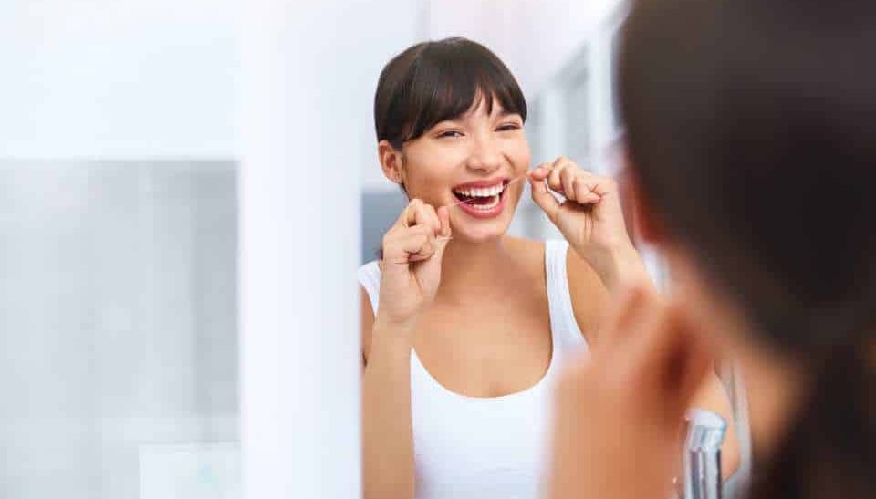 A young female flossing her teeth in the mirror