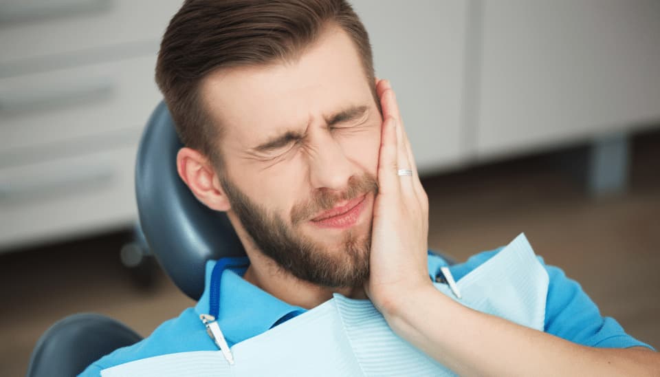 Man holding his jaw from the pain of a root canal in a dentist's chair