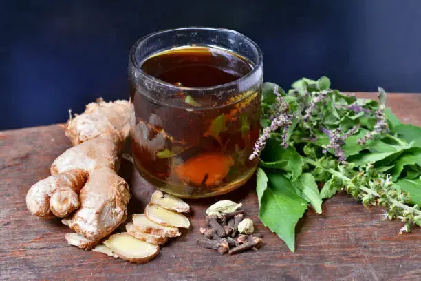 Glass cup of tea with fresh ginger, herbs, and spices, illustrating the benefits of green and black tea for stronger teeth.